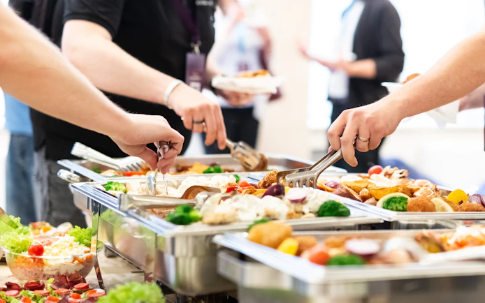 Tourists serving themselves at an all-you-can-eat buffet with diverse dishes.