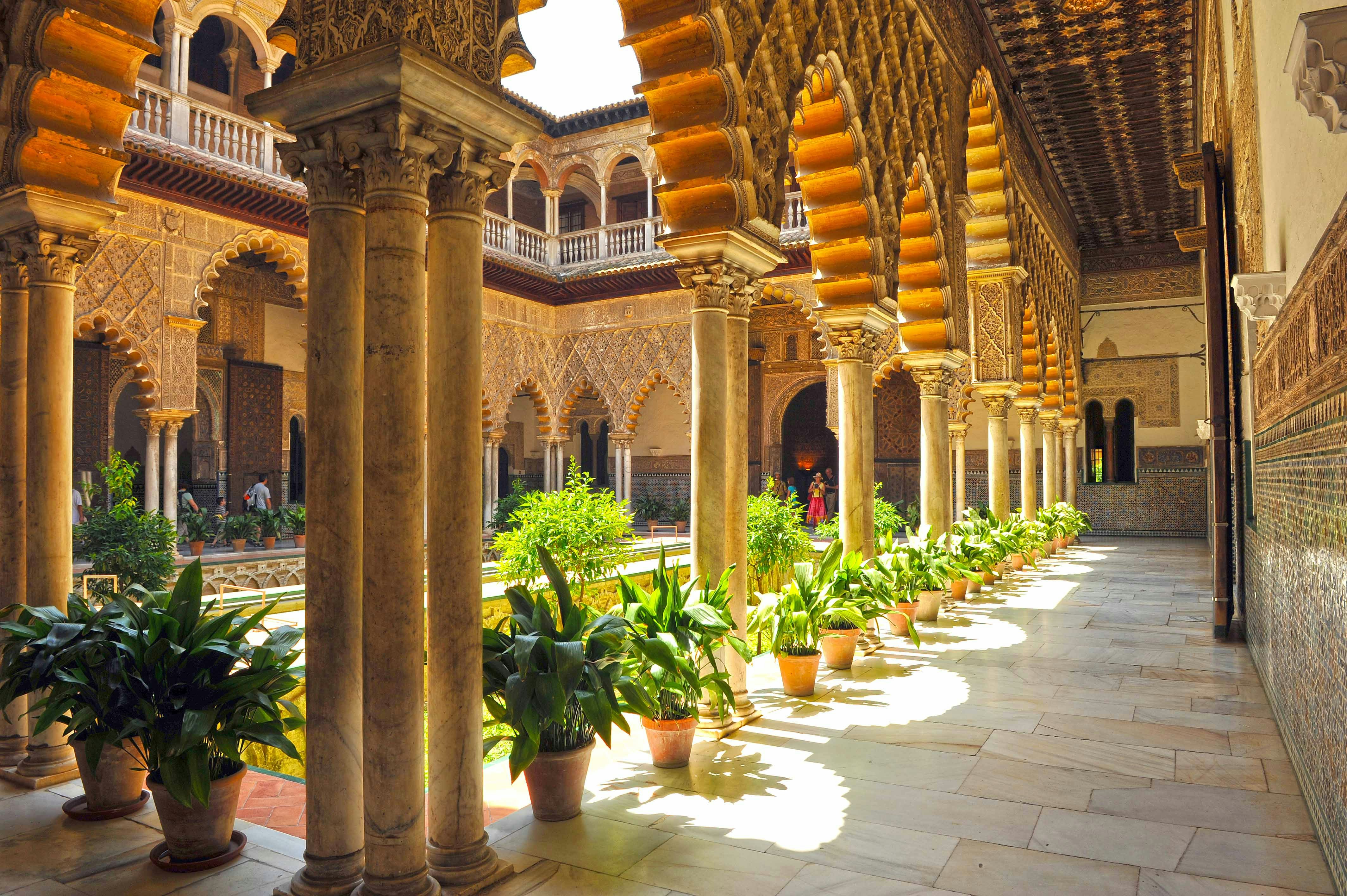 Alcazar Seville courtyard with intricate arches and lush gardens.
