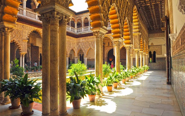 Alcazar Seville courtyard with intricate arches and lush gardens.