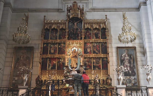 Altar inside Sagrada Familia with ornate religious artwork and visitors observing.