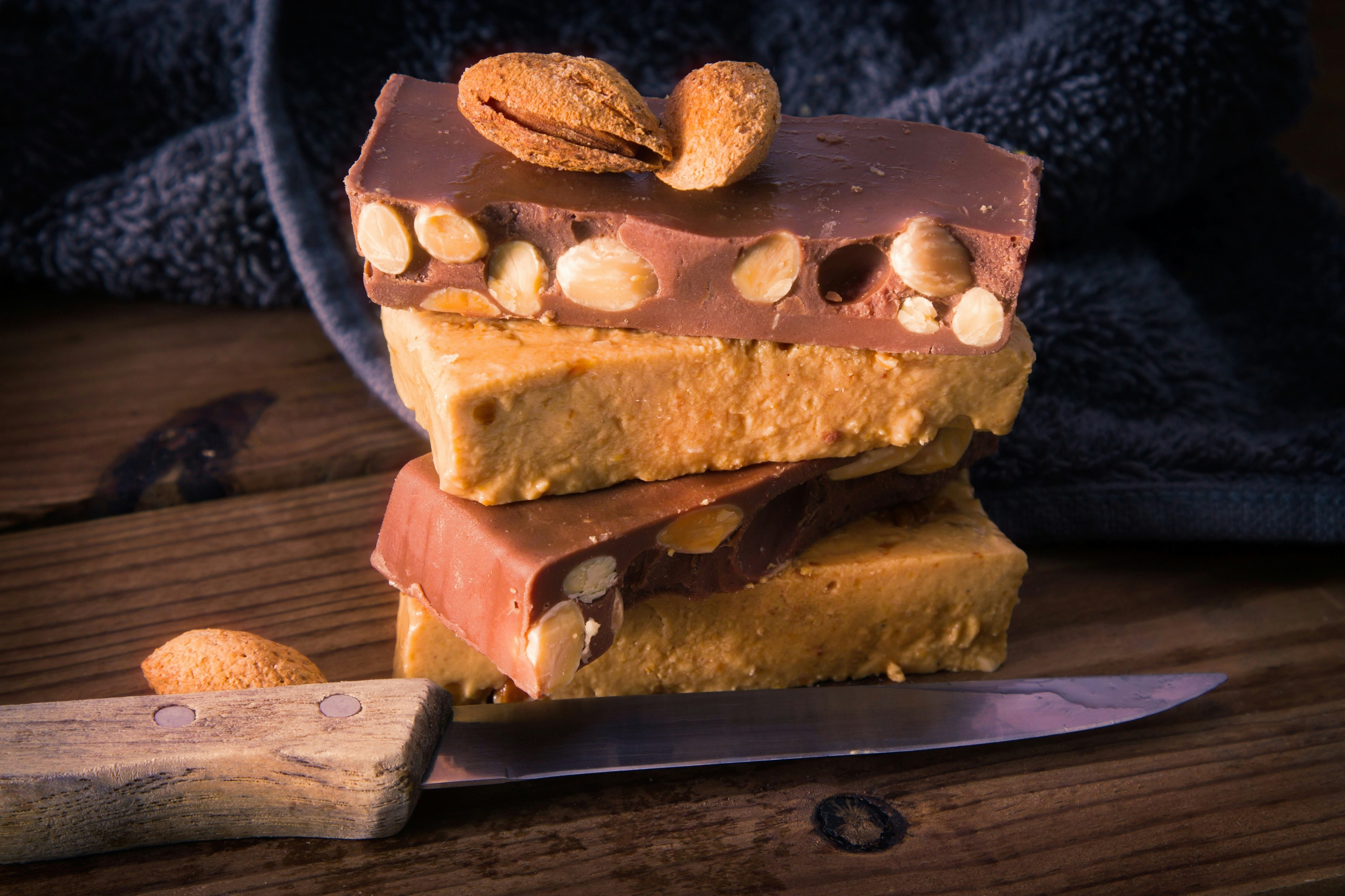 Turrón bars with almonds stacked on a wooden table next to a knife.