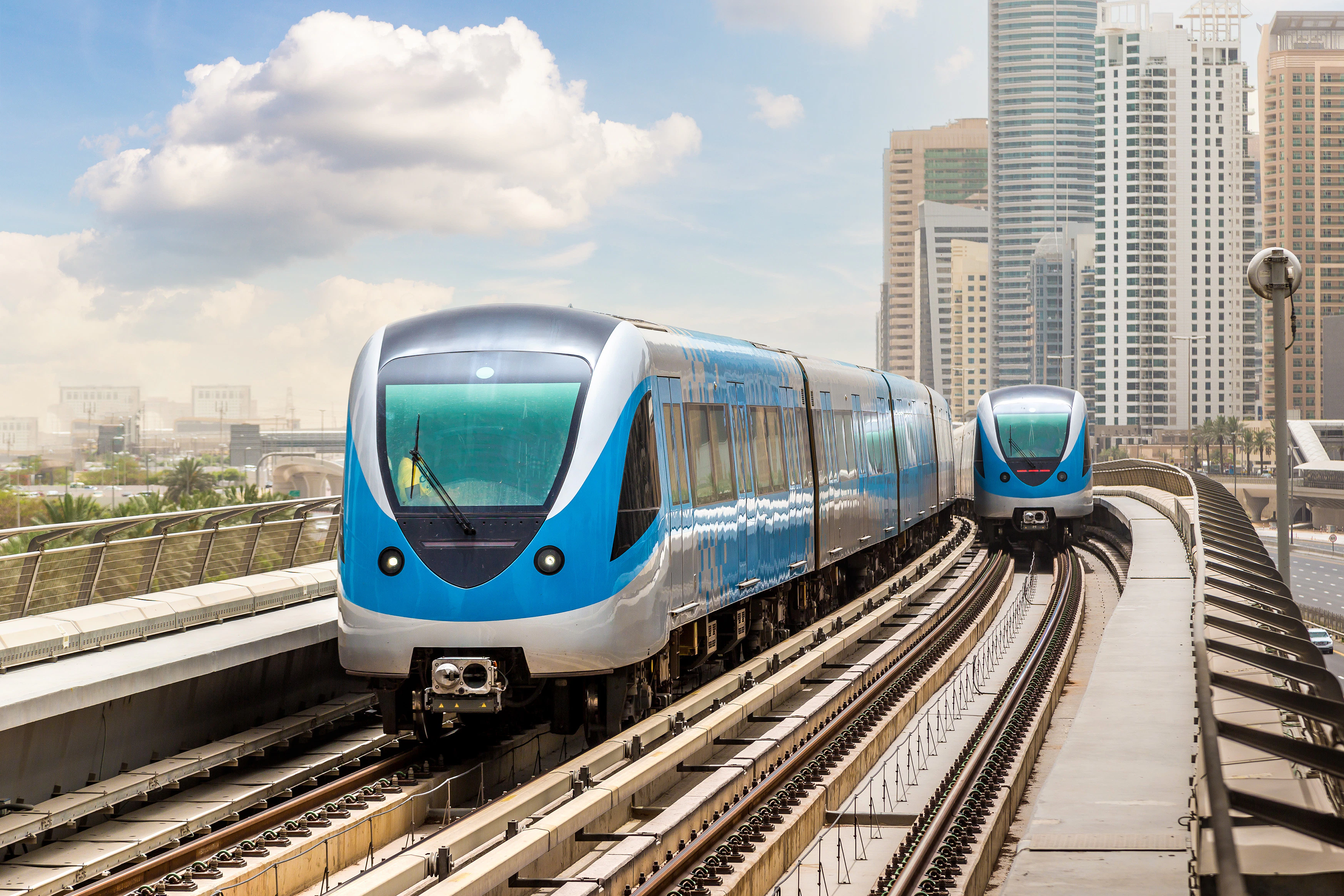 Dubai Metro trains on elevated tracks with city skyline in the background.