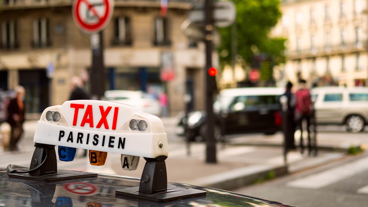 Paris taxi sign on a cab roof with blurred city street in the background.