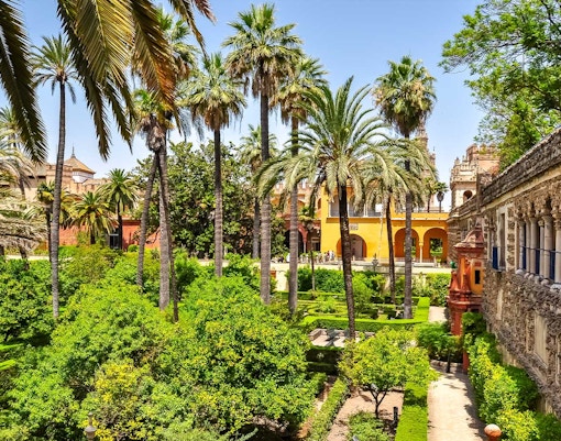 Alcazar of Seville courtyard with intricate arches and lush gardens.