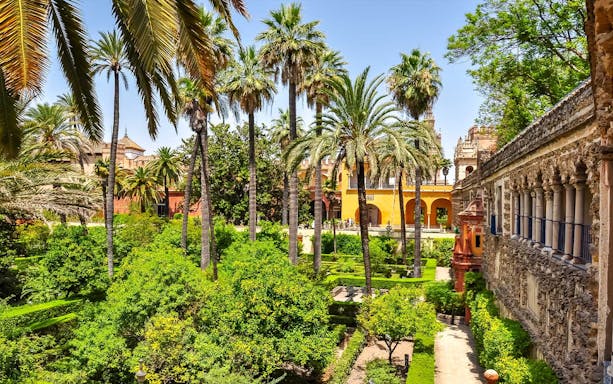 Alcazar of Seville courtyard with intricate arches and lush gardens.