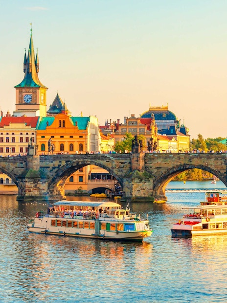 Boats on Vltava River near Charles Bridge, Prague Castle in background.