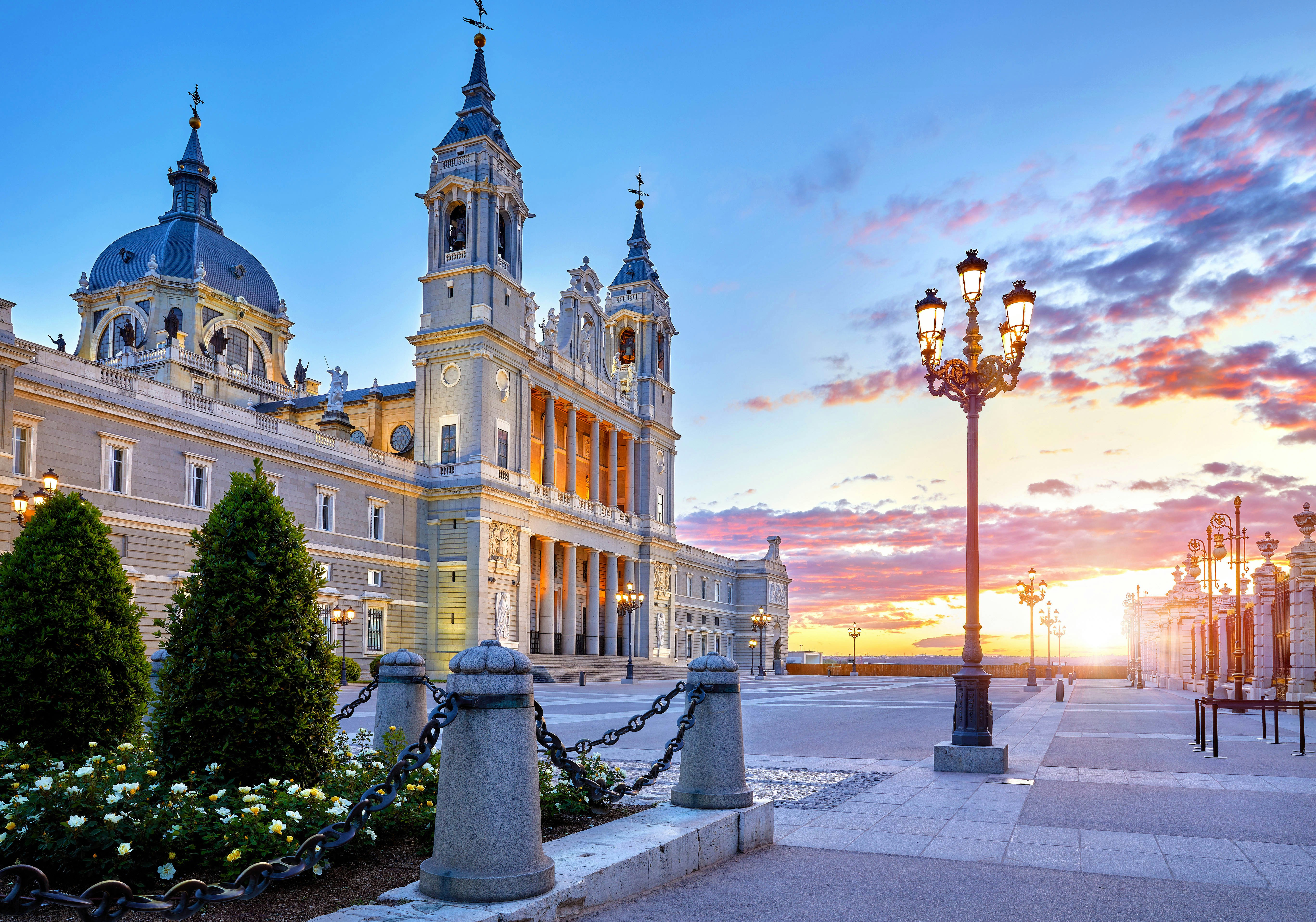 Almudena Cathedral in Madrid at sunset with ornate street lamps.
