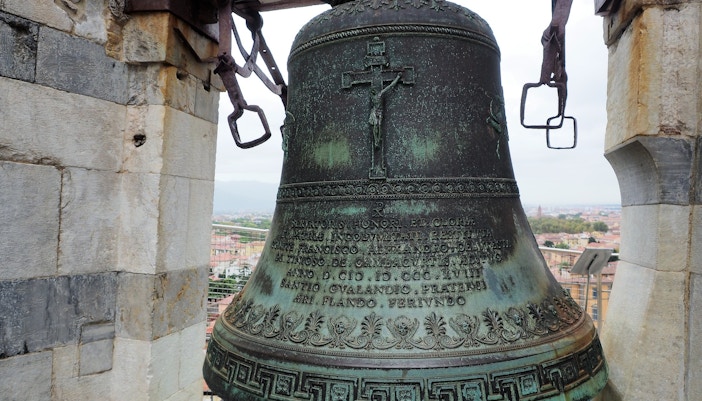 Bell at the top of the Leaning Tower of Pisa, Italy, with city view in the background.