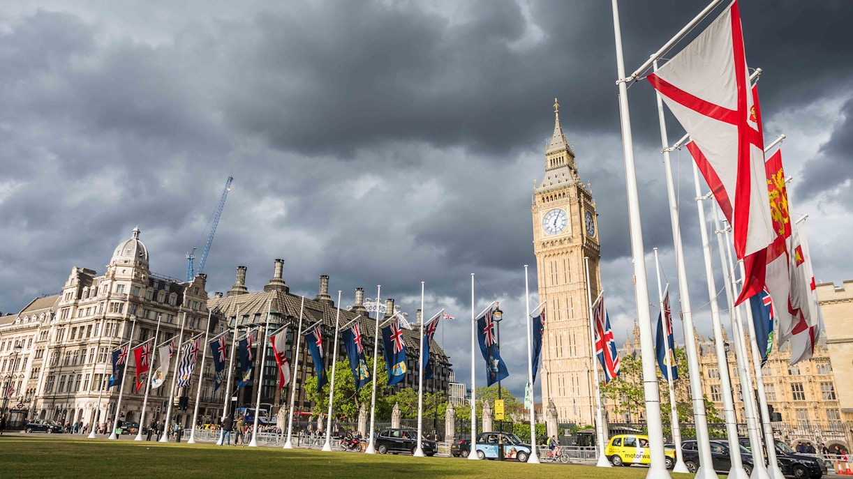 Flags and Big Ben at Parliament Square, London, on a cloudy day.