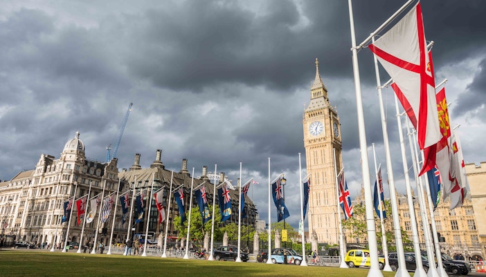 Flags and Big Ben at Parliament Square, London, on a cloudy day.