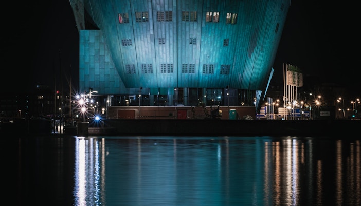 NEMO Science Museum illuminated at night, viewed from Amsterdam canal during boat tour.