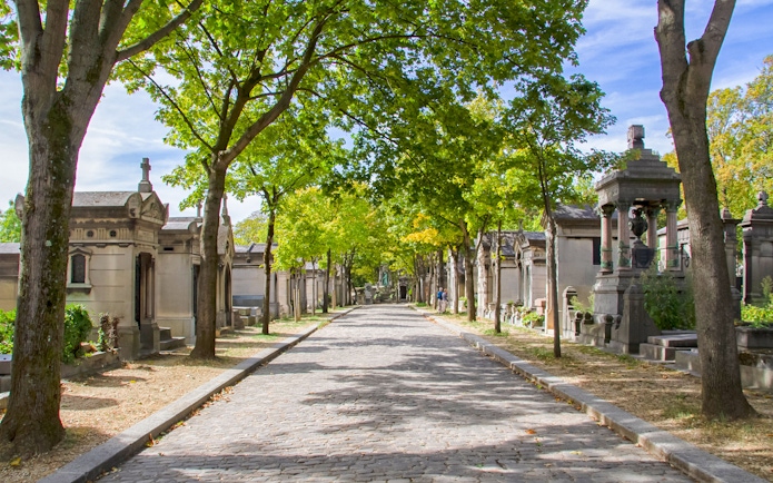 Cobbled path lined with tombs and trees at Cimetière du Père Lachaise, Paris.