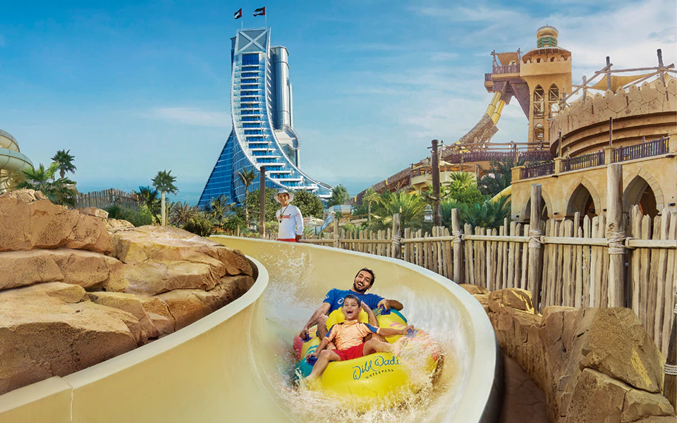 Visitors enjoying a water slide at Wild Wadi Water Park, Dubai, with Burj Al Arab in the background.