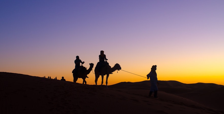 Camel ride at sunset during Dubai Desert Safari overnight tour.