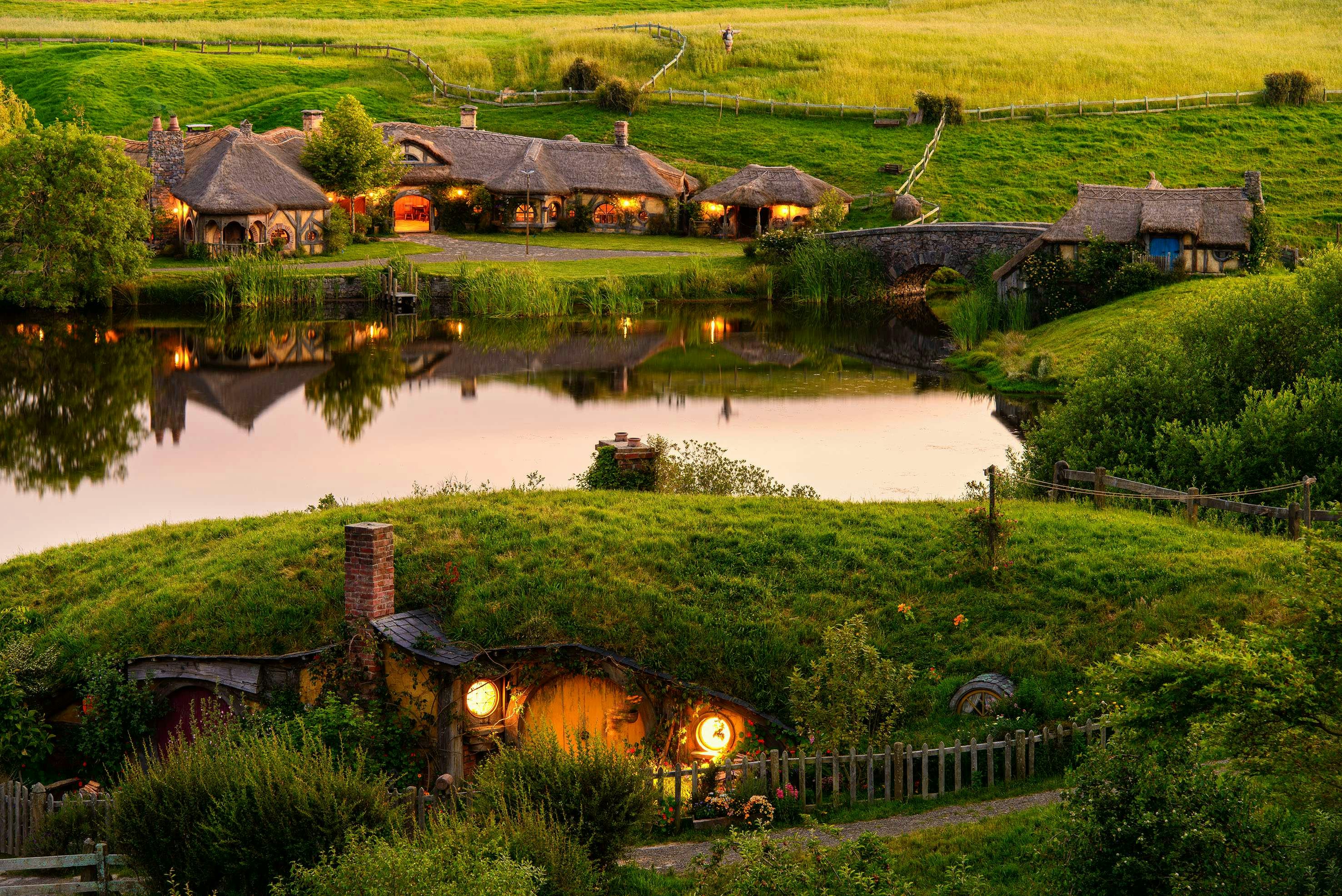 Hobbiton village with illuminated hobbit houses and a stone bridge in New Zealand.