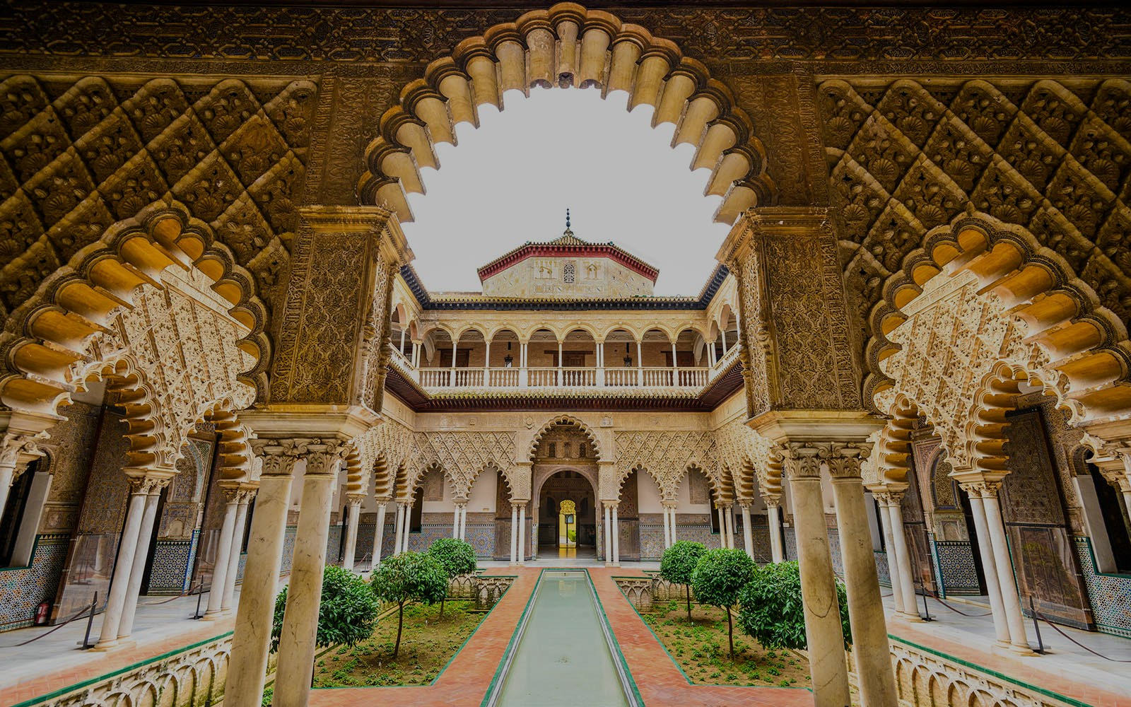 Alcazar of Seville courtyard with intricate arches and lush gardens.