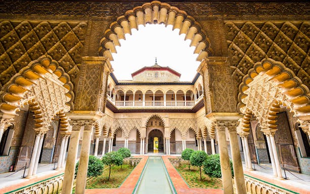 Alcazar of Seville courtyard with intricate arches and lush gardens.
