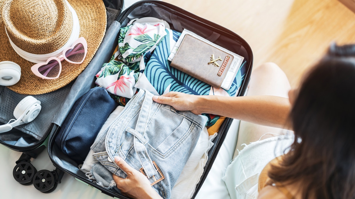 Packing suitcase with summer clothes, hat, sunglasses, and travel documents for Arachova Village.