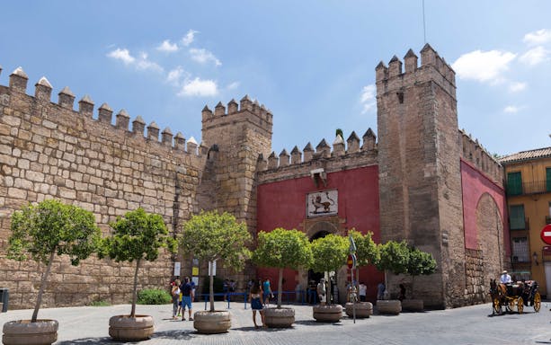 Alcazar of Seville entrance with tourists and horse-drawn carriage.