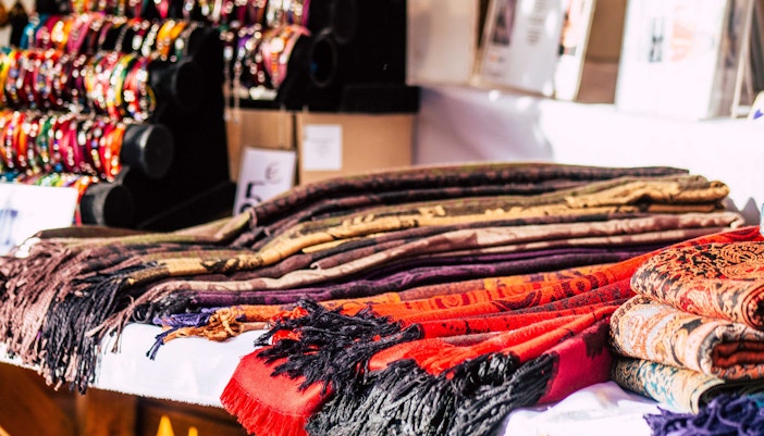 Scarves displayed at a market stall with colorful bracelets in the background.