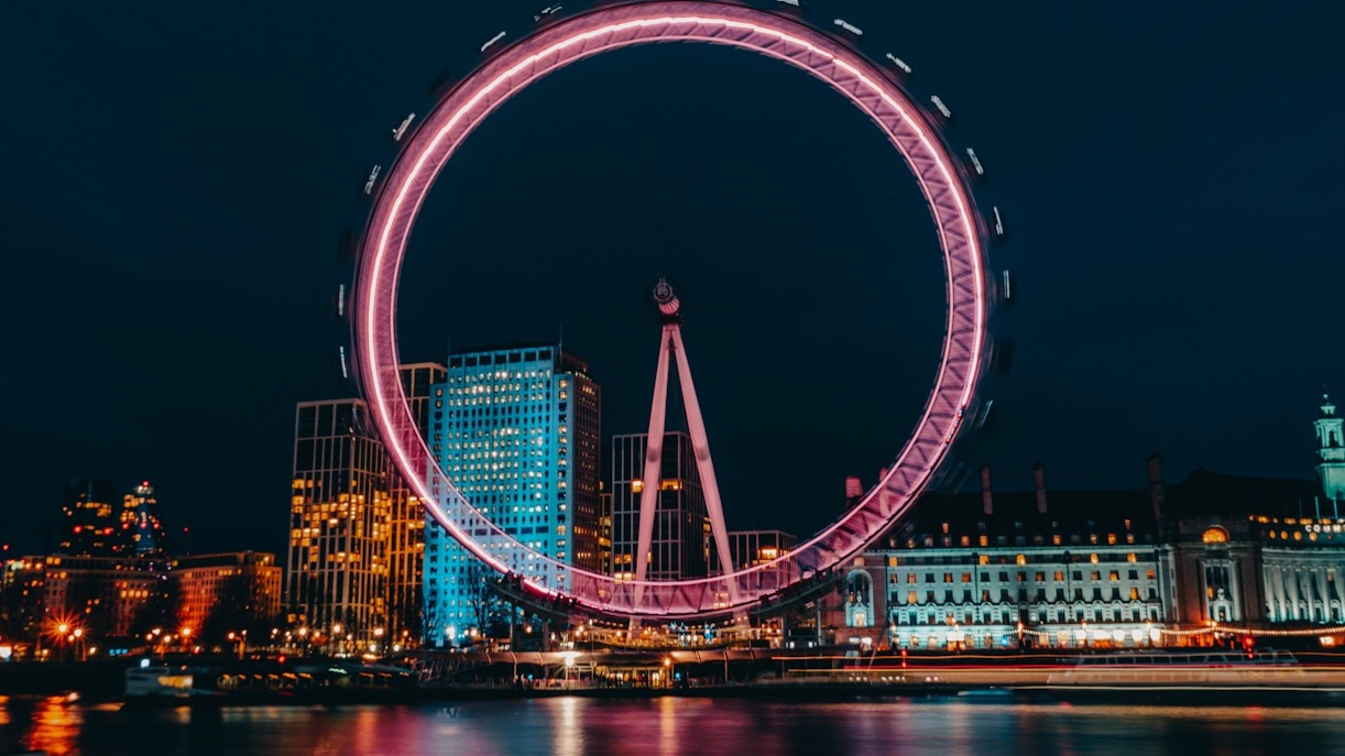 London Eye illuminated at night with city skyline in the background.
