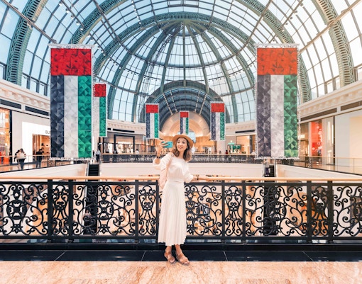 Mall of the Emirates interior with UAE flags and a visitor taking a selfie in Dubai.