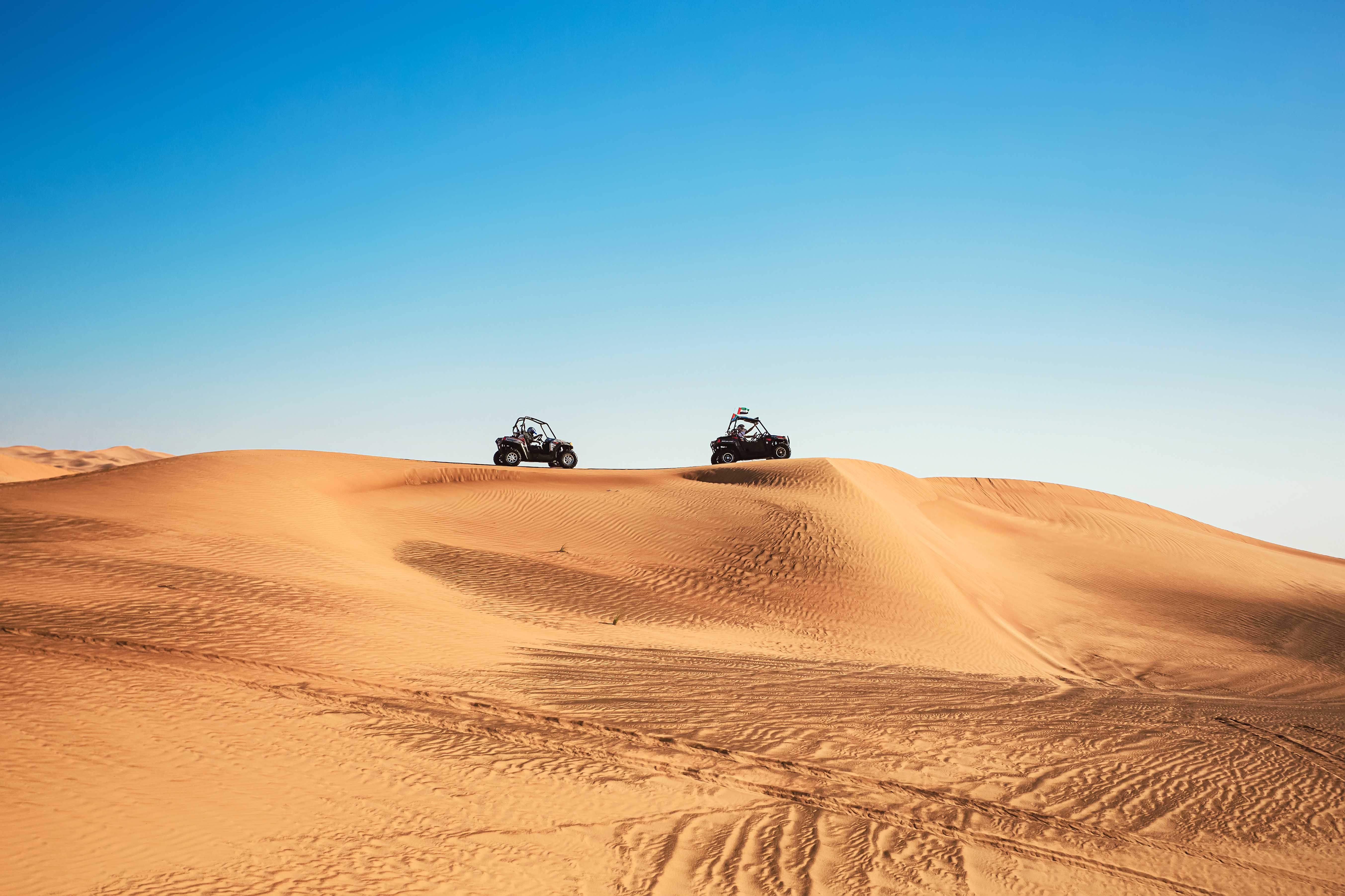 Dune buggies driving over sand dunes in Al Aweer Desert, Dubai Desert Safari.