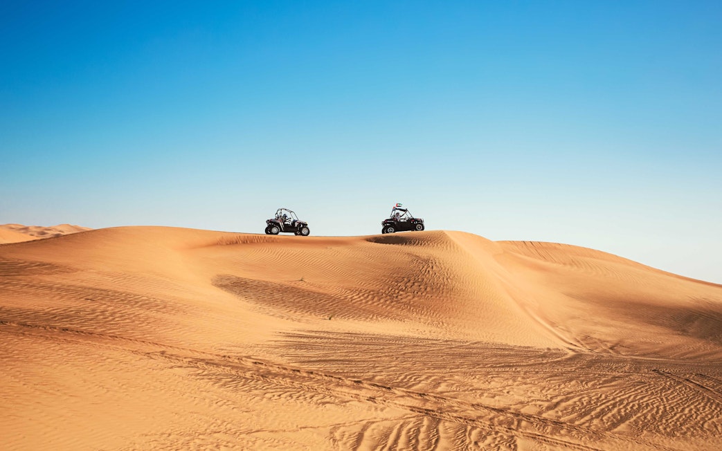 Dune buggies driving over sand dunes in Al Aweer Desert, Dubai Desert Safari.