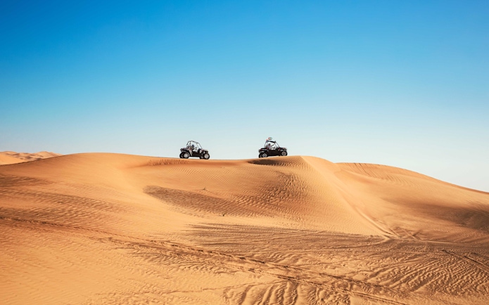 Dune buggies driving over sand dunes in Al Aweer Desert, Dubai Desert Safari.