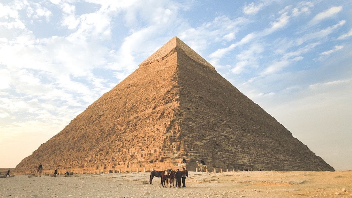Khafre Pyramid at Giza with camels in the foreground under a blue sky.
