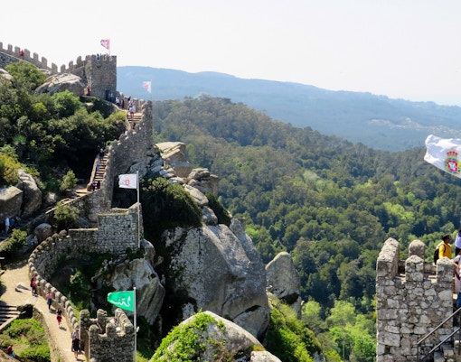 Moorish Castle in Sintra with visitors walking along the stone walls and lush forest in the background.