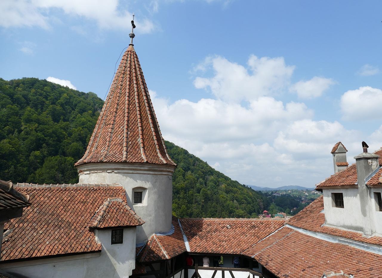 Bran Castle tower with red-tiled roof against a backdrop of green hills and blue sky.