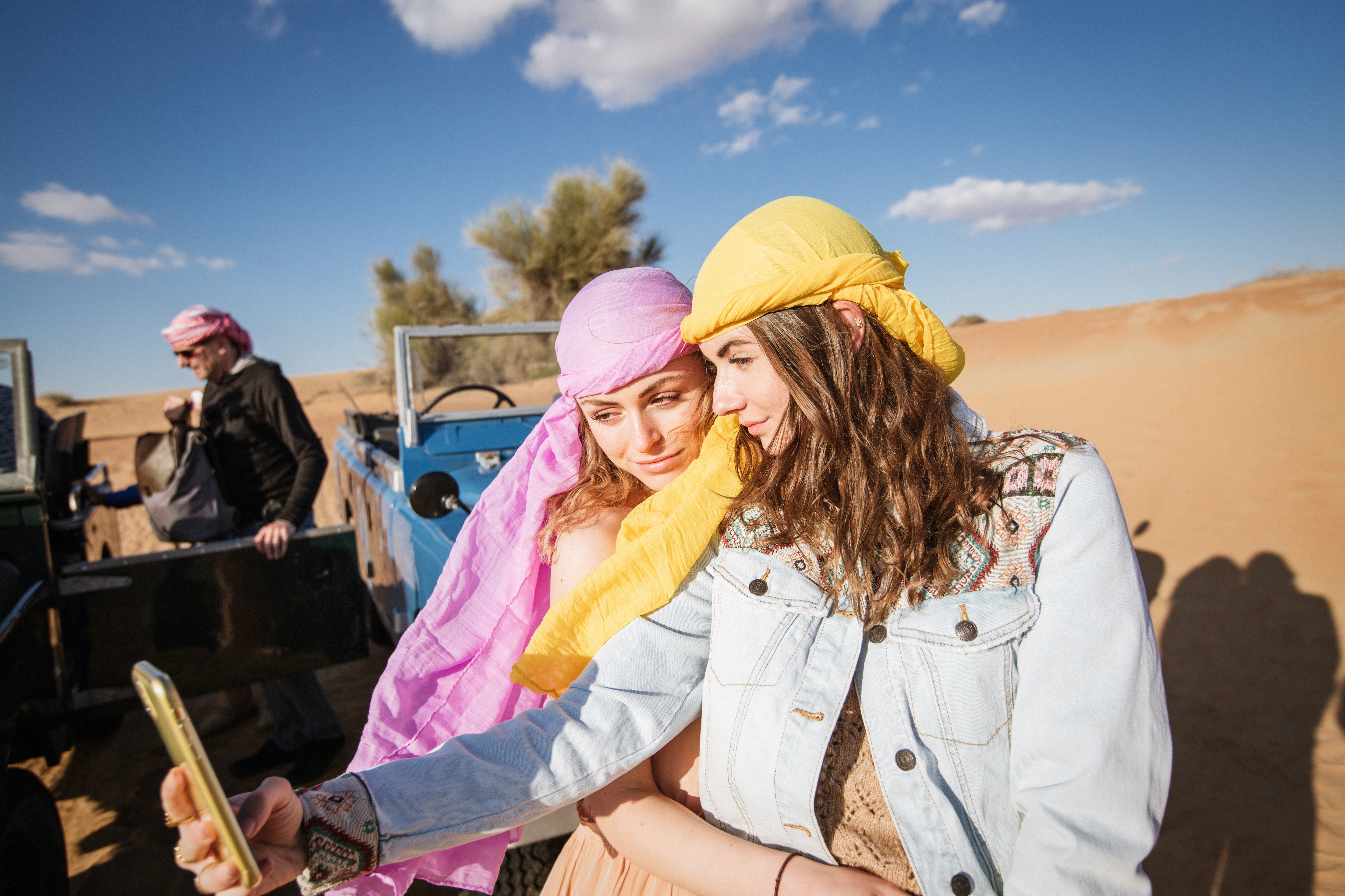 Tourists taking a selfie in the Dubai desert with vintage jeep in background.