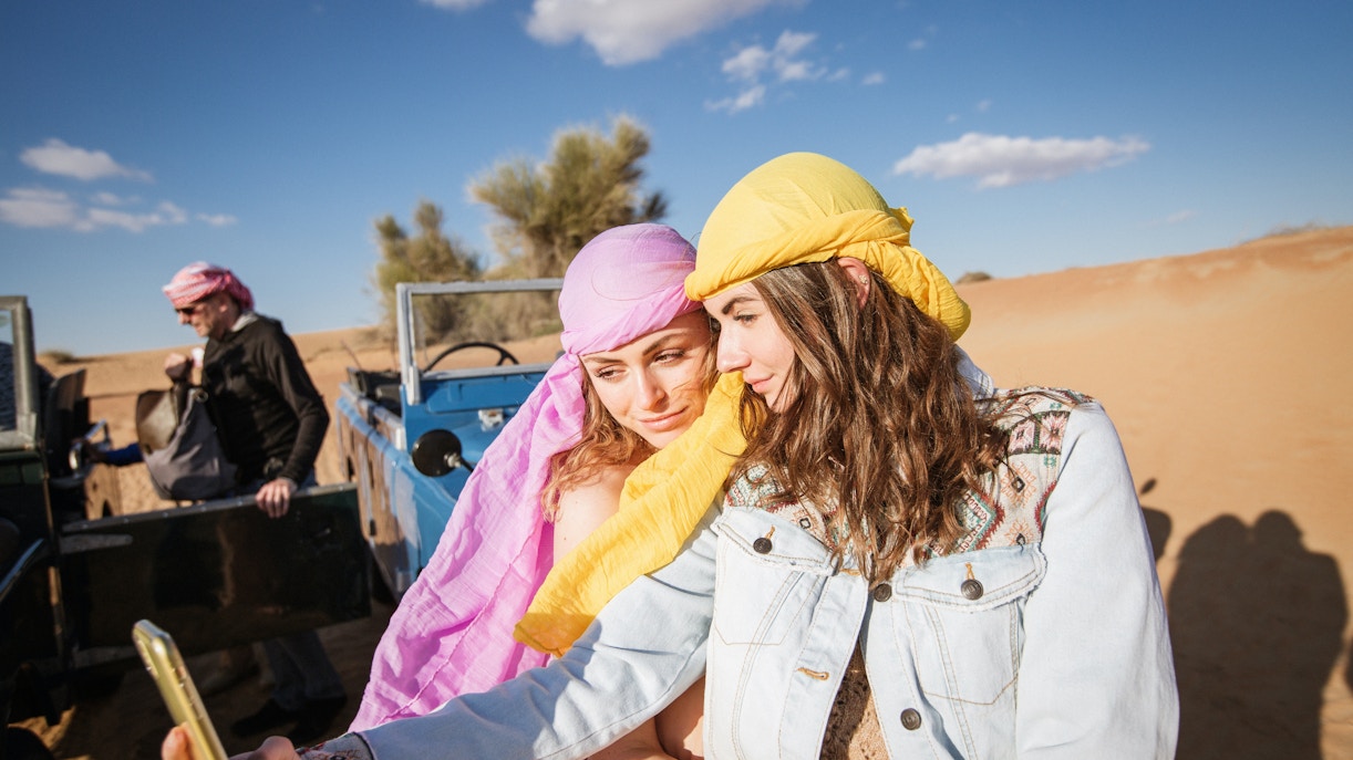 Tourists taking a selfie in the Dubai desert with vintage jeep in background.