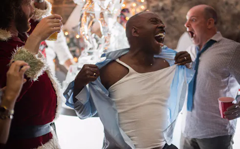 Man celebrating at office Christmas party with coworkers, ice sculpture in background.