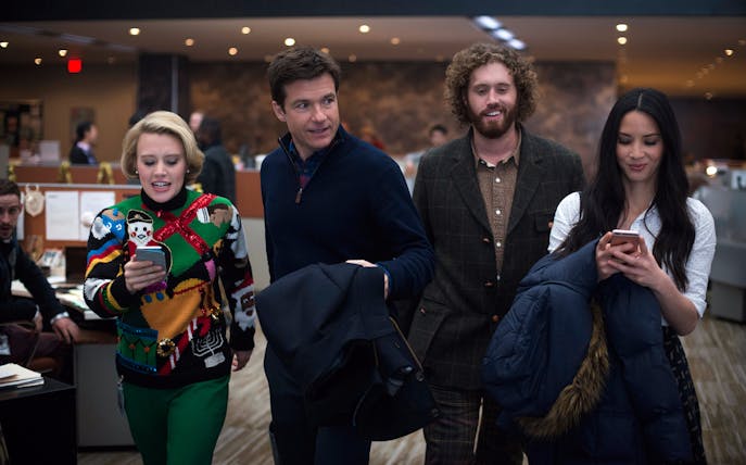Group of colleagues walking through an office during a Christmas party, holding phones and jackets.