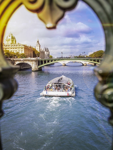 Batobus cruising on the Seine River in Paris with historic buildings and bridge in view.