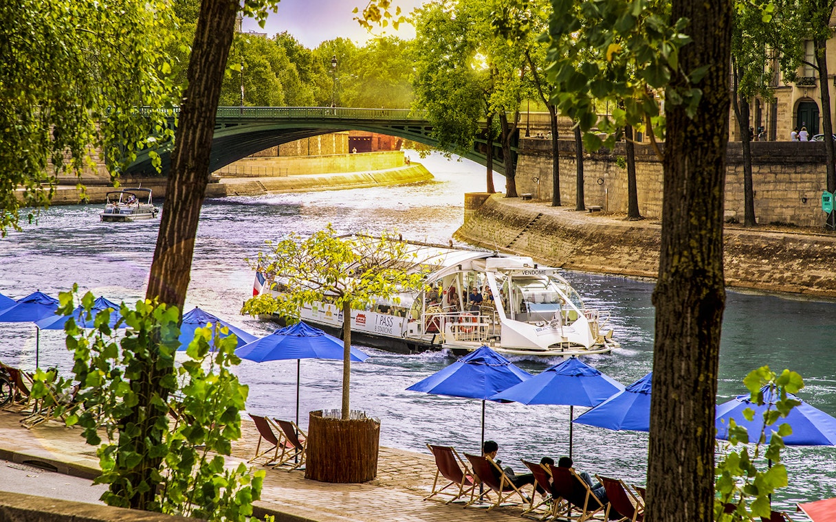 Batobus cruising on the Seine River in Paris with blue umbrellas and a bridge in view.