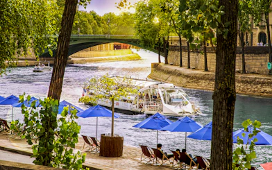 Batobus cruising on the Seine River in Paris with blue umbrellas and a bridge in view.