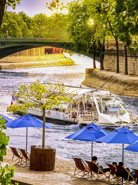 Batobus cruising on the Seine River in Paris with blue umbrellas and a bridge in view.