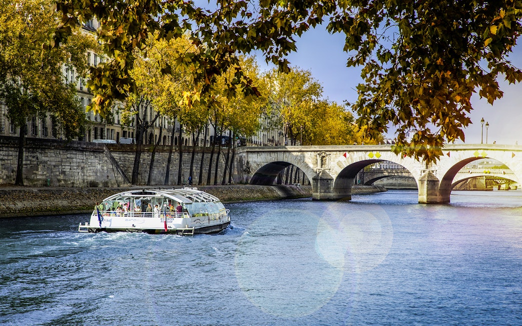 Seine River cruise boat near Paris bridge with autumn trees.