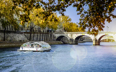 Seine River cruise boat near Paris bridge with autumn trees.