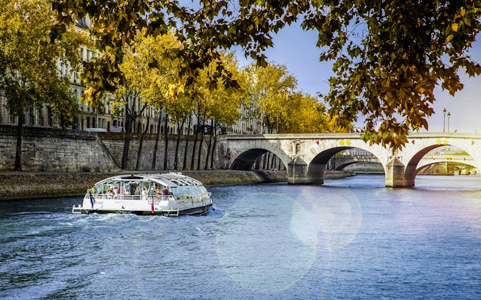 Seine River cruise boat near Paris bridge with autumn trees.