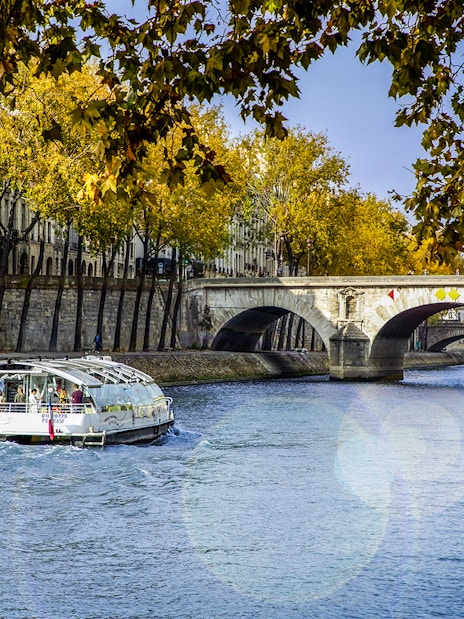 Seine River cruise boat near Paris bridge with autumn trees.