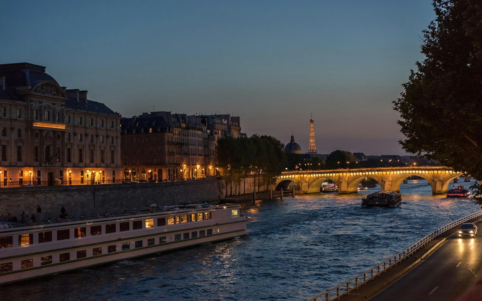 Bateaux Parisiens dinner cruise on the Seine River, Paris, with illuminated Eiffel Tower in the background.