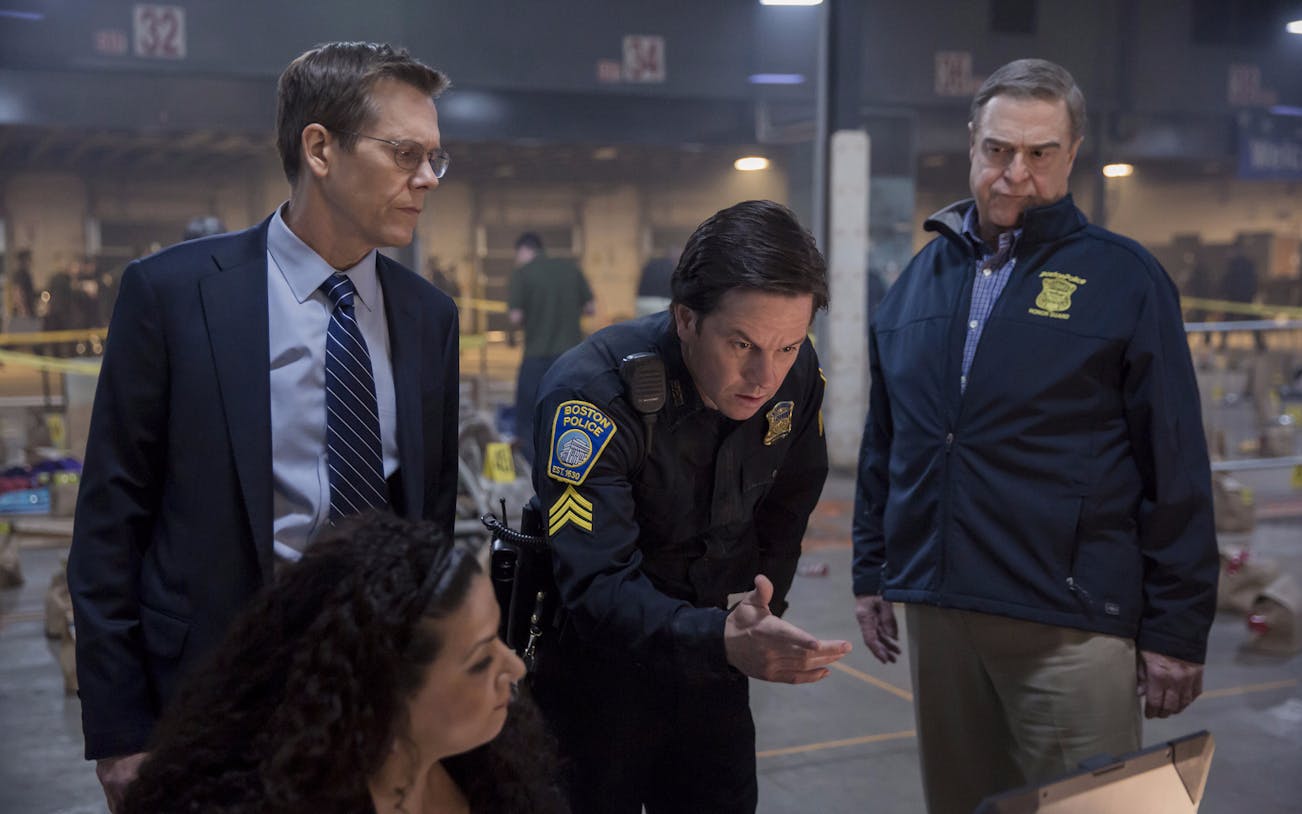 Police officers discussing a case in a dimly lit room during Patriots Day investigation.