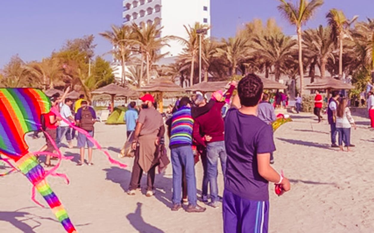 Festival attendees flying colorful kites on a sandy beach at the Bukhara Kite Festival.