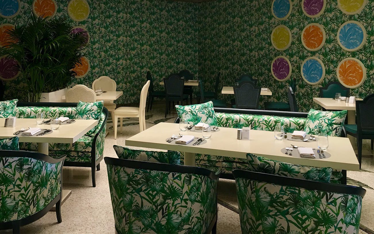 Dining setup at Giardino Restaurant, Palazzo Versace, with tropical decor and colorful wall art.