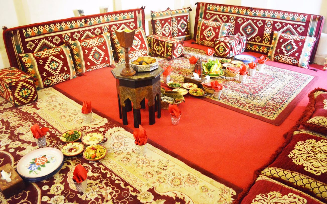 Traditional seating area with patterned cushions and a variety of dishes at Barjeel Al Arab, Barjeel Heritage Guest House.