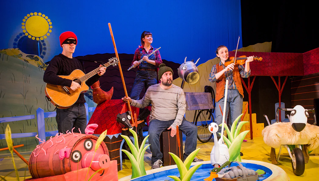 Stage performance of "What The Ladybird Heard" with actors and farm animal props.